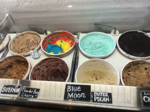 A display of various ice cream flavors in tubs, including Blue Moon, Butter Pecan, and others, with colorful swirls.