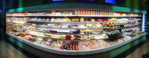 A wide display of various cheeses and dairy products arranged neatly in a well-lit refrigerated case.