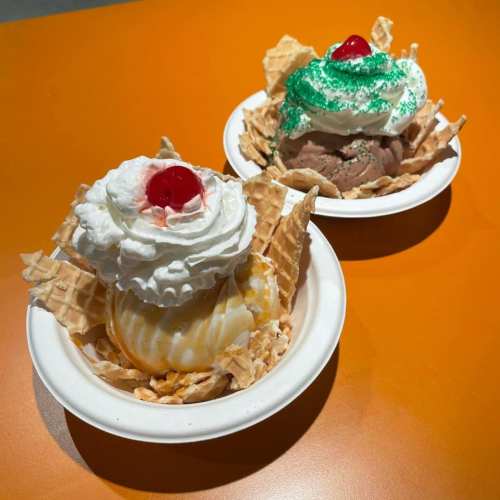 Two ice cream sundaes in bowls, one with whipped cream and a cherry, the other topped with green sprinkles.