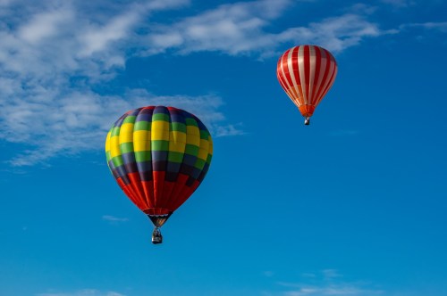 Two colorful hot air balloons float against a bright blue sky with scattered clouds.