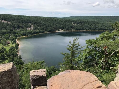 A scenic view of a calm lake surrounded by lush green trees and hills under a partly cloudy sky.