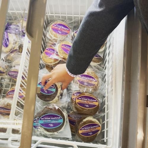 A hand reaching for an ice cream sandwich in a freezer filled with packaged treats.