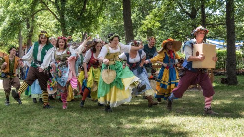 A group of performers in colorful costumes joyfully dancing together in a park setting.