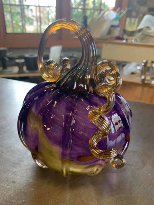 A decorative glass pumpkin in purple and yellow with swirling, elegant tendrils on top.