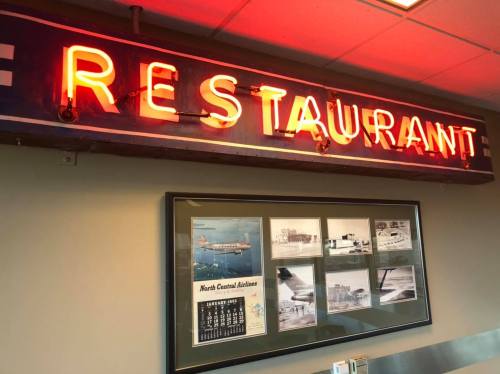 Neon "RESTAURANT" sign above framed historical photos of North Central Airlines.
