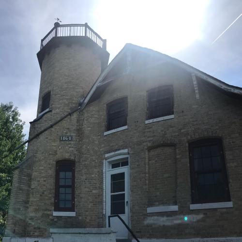 Historic building with a lighthouse tower, marked "1868," under a bright sky.