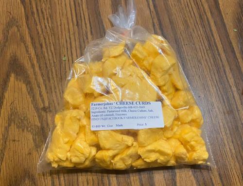 A clear bag of yellow cheese curds on a wooden table, labeled with ingredients and price.