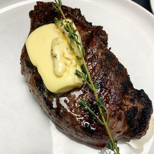 A perfectly cooked steak topped with a pat of butter and garnished with fresh thyme on a white plate.
