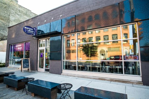 Exterior of a modern building with large windows, featuring a sign that reads "Purple Door" and an "Open" sign.