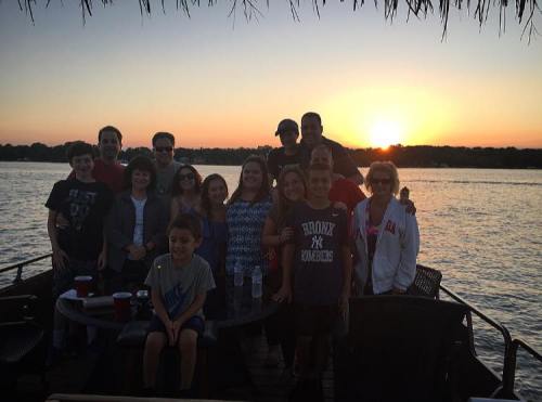 A group of people poses together on a dock at sunset, with water and trees in the background.