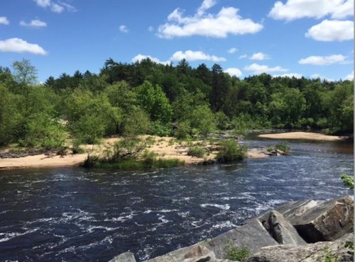 A serene river flows through a lush green landscape under a blue sky with fluffy clouds.