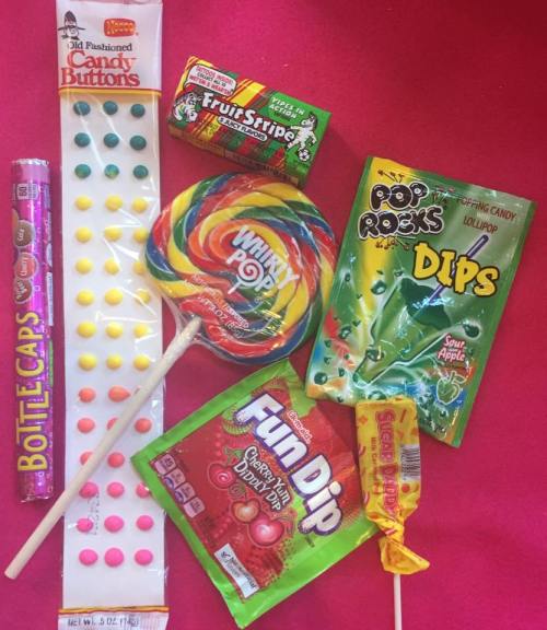 A colorful assortment of candies including lollipops, Fun Dip, Pop Rocks, and Candy Buttons on a bright pink background.