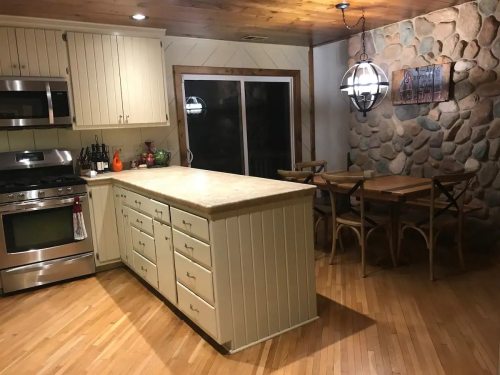 A cozy kitchen with a central island, stainless steel appliances, and a stone wall, featuring a dining table nearby.
