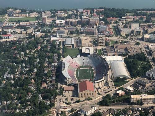 Aerial view of a stadium surrounded by buildings and greenery, near a body of water.
