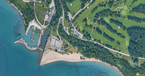 Aerial view of a marina, beach, and golf course along a coastline with green spaces and water.