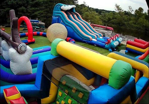 Colorful inflatable obstacle course set up near a lake, featuring slides, tunnels, and various climbing structures.