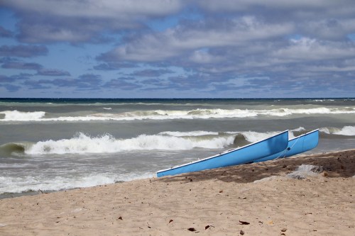 Two blue canoes on a sandy beach with waves and cloudy skies in the background.