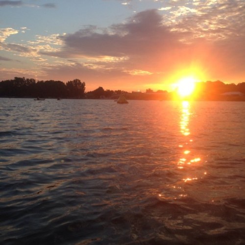 Sunset over a calm lake, with vibrant orange and yellow hues reflecting on the water's surface.
