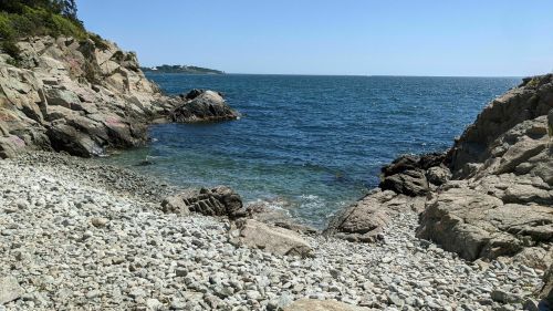 A rocky shoreline with clear blue water and a distant island under a bright blue sky.