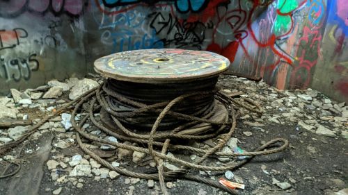 A large spool of thick rope sits on a rocky floor, surrounded by colorful graffiti on the walls.
