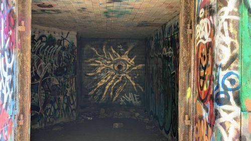 A dimly lit room covered in colorful graffiti, featuring an eye symbol on the back wall.
