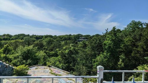 A scenic view of lush green trees under a blue sky, with a distant building visible among the foliage.