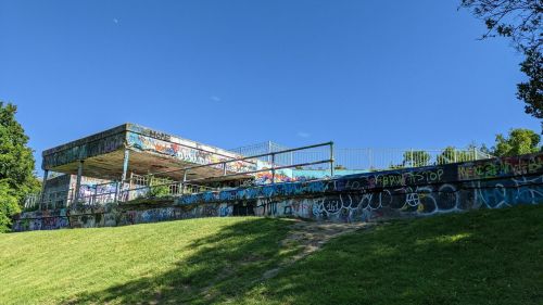 Abandoned building covered in colorful graffiti, set against a clear blue sky and green grass.