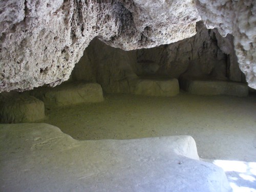 A dimly lit cave interior with smooth stone benches and rough, textured walls.