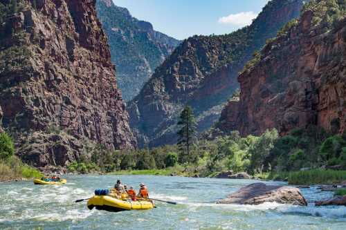 A group of people in yellow rafts navigate a river surrounded by steep, rocky cliffs and lush greenery.