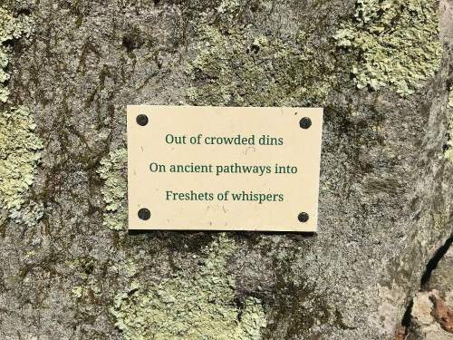 A sign on a mossy rock reads: "Out of crowded dins, On ancient pathways into, Freshests of whispers."