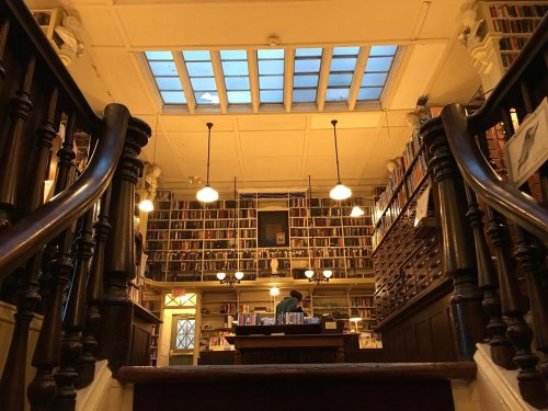 A cozy library interior with wooden stairs, tall bookshelves, and warm lighting, creating an inviting atmosphere.