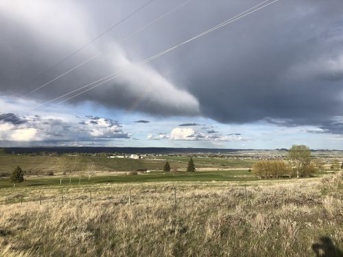 A scenic landscape featuring rolling hills, a rainbow, and dramatic clouds under a partly cloudy sky.