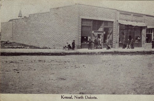 Historic photo of a building in Kensal, North Dakota, with people and children gathered outside.