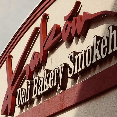 Sign for "Kraków Deli Bakery Smoked" with bold red lettering on a light background.
