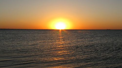 A serene sunset over calm waters, with the sun glowing brightly on the horizon.