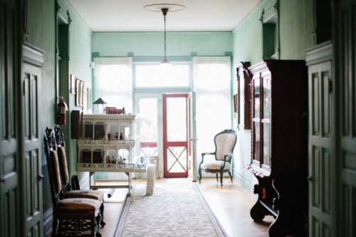 A bright hallway with mint green walls, vintage furniture, and large windows, creating a welcoming atmosphere.