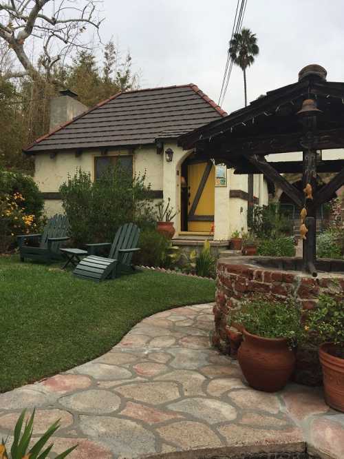 A charming cottage with a yellow door, surrounded by greenery and a stone pathway leading to a rustic well.