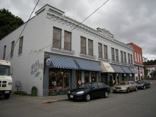 Historic building with striped awnings, shops on the ground floor, and parked cars in front under a cloudy sky.