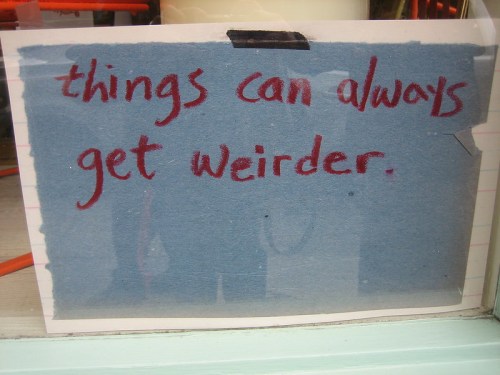 A handwritten sign on blue paper reads, "things can always get weirder."