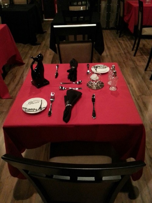 A table set for dining with red tablecloth, elegant plates, silverware, and a decorative centerpiece.