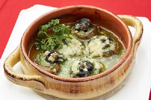 A clay dish filled with baked escargot in garlic butter, garnished with parsley.