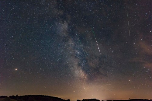 A starry night sky filled with the Milky Way and multiple shooting stars streaking across the scene.