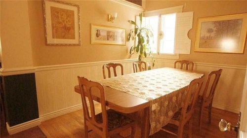 A cozy dining room with a wooden table, chairs, and framed artwork on the walls, illuminated by natural light.