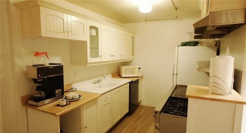 A small kitchen featuring white cabinets, a sink, coffee maker, microwave, and a stainless steel stove.