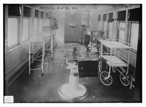 Interior of a vintage hospital car, featuring medical equipment and empty hospital beds, with large windows for natural light.