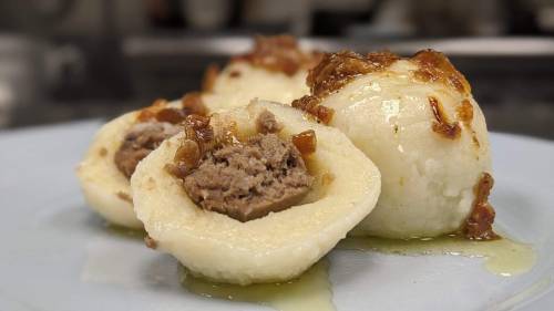 Three dumplings filled with meat, topped with caramelized onions, served on a light blue plate.