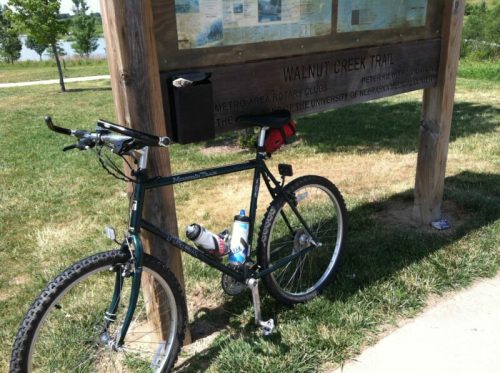 A mountain bike parked next to a sign for Walnut Creek Trail, surrounded by grass and trees.