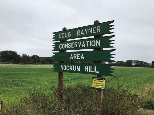 Signpost indicating "Doug Rayner Conservation Area" and "Nockum Hill," with a notice about dogs and vehicles.