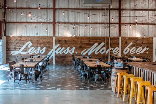 Interior of a brewery with wooden walls, tables, and a sign that reads "Less fuss. More beer." in a casual setting.