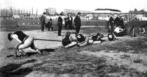 Historical photo of athletes competing in a tug-of-war event, with spectators watching in the background.